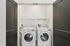 Modern laundry closet with sleek black doors featuring a high-efficiency washer and dryer combo, complete with a convenient storage shelf.