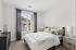 Bright and inviting bedroom featuring a cozy bed with soft green accents, stylish dressers, and a large window with elegant curtains.