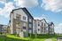 Modern apartment complex with sleek design, spacious balconies, and lush green surroundings under a bright blue sky.