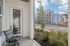 Inviting porch area with a cozy chair, overlooking a modern apartment complex and a well-maintained garden.