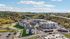 Aerial view of a contemporary apartment complex surrounded by lush greenery and scenic hills, featuring modern architecture and ample parking.