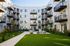 Modern apartment complex with sleek balconies overlooking a lush, green courtyard featuring cozy outdoor seating and vibrant landscaping.