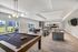 Modern and inviting common area featuring plush gray seating, a stylish round dining table with chairs, artistic wall decor, and a sleek billiards table under contemporary lighting.
