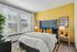 Vibrant bedroom with a bold yellow accent wall, plush pillows, and large windows allowing abundant natural light.