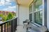 Charming apartment balcony with stylish wicker furniture, offering a sunny view of lush greenery and elegant buildings.