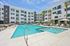 Luxurious apartment complex featuring a sparkling pool, modern design, and spacious balconies under a clear blue sky.