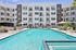Luxurious apartment complex featuring a sparkling swimming pool surrounded by stylish loungers and lush palm trees, offering a perfect blend of relaxation and modern living.