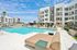 Luxurious apartment complex with sparkling pool, modern lounge chairs, and stylish architecture under a vibrant blue sky.