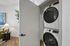 Modern apartment featuring a sleek laundry closet with a stacked washer and dryer, complemented by chic decor and a cozy side table with a lamp.