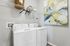Chic and functional laundry room featuring modern washer and dryer, stylish artwork, and ample shelving space for organization.