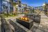 Luxurious apartment complex featuring a modern fire pit, inviting outdoor seating, palm trees, and a sparkling pool under an evening sky.