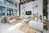 Luxurious apartment living area featuring modern gray sofas, vibrant decor, and a large wall-mounted TV, set against expansive windows offering natural light.