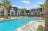 Luxurious apartment complex with a pristine swimming pool, surrounded by lush palm trees and modern architecture.
