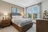 Elegant bedroom with a cozy wooden bed, soft bedding, and stylish decor, illuminated by natural light streaming through large windows with a garden view.
