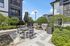 Inviting outdoor patio with modern seating, surrounded by lush greenery, featuring built-in BBQ grills under a bright blue sky.