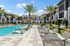 Luxury apartment complex showcasing a pristine swimming pool surrounded by lush palm trees and stylish lounge chairs, offering a resort-style living experience.