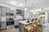 Contemporary kitchen and living area with sleek grey cabinets, modern appliances, and cozy seating, bathed in natural light.