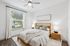 Bright and inviting bedroom with modern wooden bed frame, cozy white linens, and a stylish ceiling fan, illuminated by natural light through a large window.