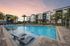 Contemporary apartment complex with lush palm trees surrounding a sparkling swimming pool at sunrise, offering a luxury resort-like ambiance.