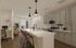 Modern kitchen and living area with elegant pendant lighting, sleek countertops, and integrated workspace, perfect for comfortable urban living.