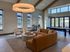 Modern, sunlit lounge featuring a plush sectional sofa, elegant round table, cozy armchairs, and expansive windows with a view.