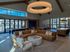 Modern open-concept living area with elegant lighting, plush seating, and expansive windows overlooking outdoor seating.