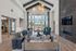 Elegant living room with vaulted ceilings, modern chandelier, and floor-to-ceiling windows offering a scenic view. Cozy seating and stylish decor create a welcoming atmosphere.