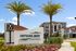 Charming entrance to Integra Myst apartments surrounded by lush landscaping and palm trees, showcasing distinctive modern architecture.
