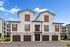 Modern apartment building with stylish exterior featuring red and white paneling, multiple garages, and inviting entryway under a clear blue sky.
