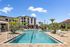 Luxurious apartment complex featuring a stunning pool with sun loungers, surrounded by lush landscaping under a bright blue sky.
