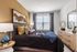 Elegant bedroom with contemporary decor, featuring a plush bed with colorful cushions, modern artwork, large window with drapes, and stylish furnishings.