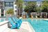 Luxury apartment outdoor pool area with stylish blue lounge chairs, vibrant cabanas, and lush palm trees in a serene, modern setting.