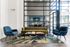 Modern apartment lobby with stylish velvet furniture, large windows, and a vibrant leaf-patterned rug.