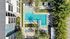 Aerial view of luxurious apartment complex with sparkling L-shaped pool, surrounded by lush greenery and colorful lounge chairs, offering a serene oasis for relaxation.