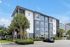 Modern apartment building with sleek design, surrounded by lush palm trees and ample parking space under a clear blue sky.