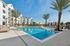 furnished outdoor pool area with palm trees and apartment building in background on sunny day