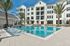 furnished outdoor pool area with palm trees and apartment building in background on sunny day