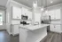 2-Bedroom Homes for Rent in Opelika, AL - Champions Square - Gourmet Kitchen with Luxury Vinyl Plank Flooring, Kitchen Island, Pendant Lights, Granite Countertops, Ceramic Tile Backsplash, White Cabinetry, and Stainless-Steel Appliances.
