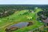 Aerial view of a lush golf course surrounded by trees and homes, featuring well-maintained greens and a serene pond.