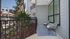 Charming apartment balcony with modern chairs, a striped rug, and lush greenery view.