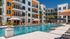 Elegant apartment complex with a central swimming pool, surrounded by modern architecture and palm trees.