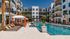 Elegant apartment complex with a pristine swimming pool surrounded by chic lounge chairs and palm trees.