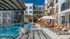Modern apartment complex with palm trees and sunlit swimming pool surrounded by orange cabanas and lounge chairs.