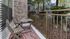 Inviting patio with wooden chairs and table, surrounded by lush greenery and modern architecture.