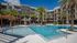 Luxurious apartment complex with a pristine swimming pool, surrounded by palm trees and modern architecture.