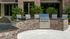 Chic outdoor kitchen with a brick bar counter and built-in stainless steel grill, complemented by modern seating and lush greenery.