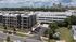 Aerial view of a modern apartment complex with lush landscaping and ample parking, set against a vibrant city skyline.