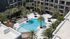 Aerial view of a luxurious apartment complex featuring a stunning swimming pool, surrounded by palm trees and leisure seating.