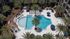 Aerial view of a luxurious apartment complex pool surrounded by palm trees and sun loungers.