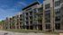 Stylish four-story apartment building with balconies and palm trees, set against a clear blue sky.